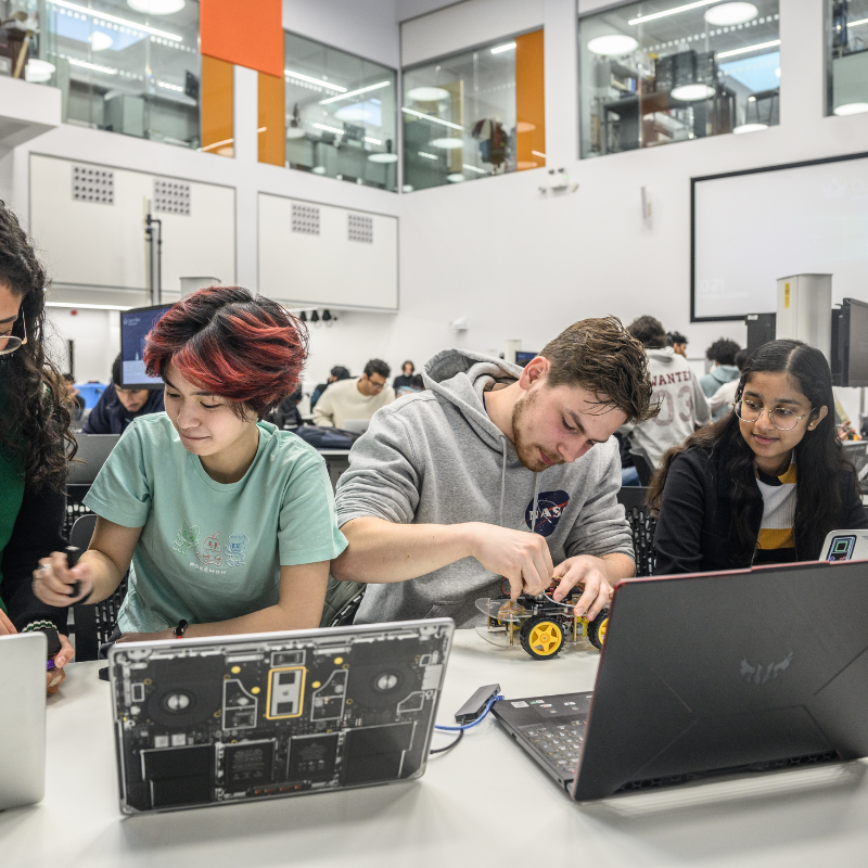 Students sit behind laptops and build toy cars