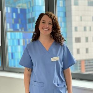 Claire wearing blue gown in front of window with Royal London Hospital building in background