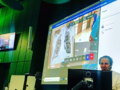 The live feed is displayed on the projector in the lecture theatre, complete with the patient's x-ray images