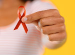 Woman holding up a red ribbon, the universal symbol of awareness and support for people living with HIV. Credit: katleho Seisa/iStock.com