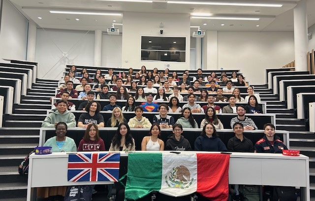 79 students sitting in rows in a lecture theatre with the Union Jack and Mexican flags on the table in front of them,