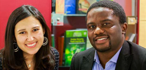 Two people smiling and sitting in front of shelves with colourful books
