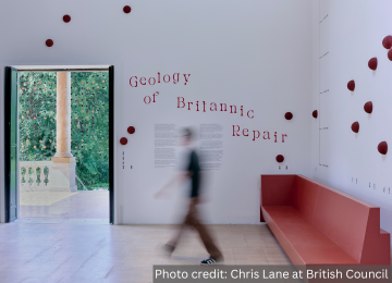 A blurred figure walks through a white room with colourful dots on the wall. Credit: Chris Lane at British Council