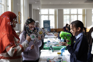A child laughs and shoots a bubble gun at two adults
