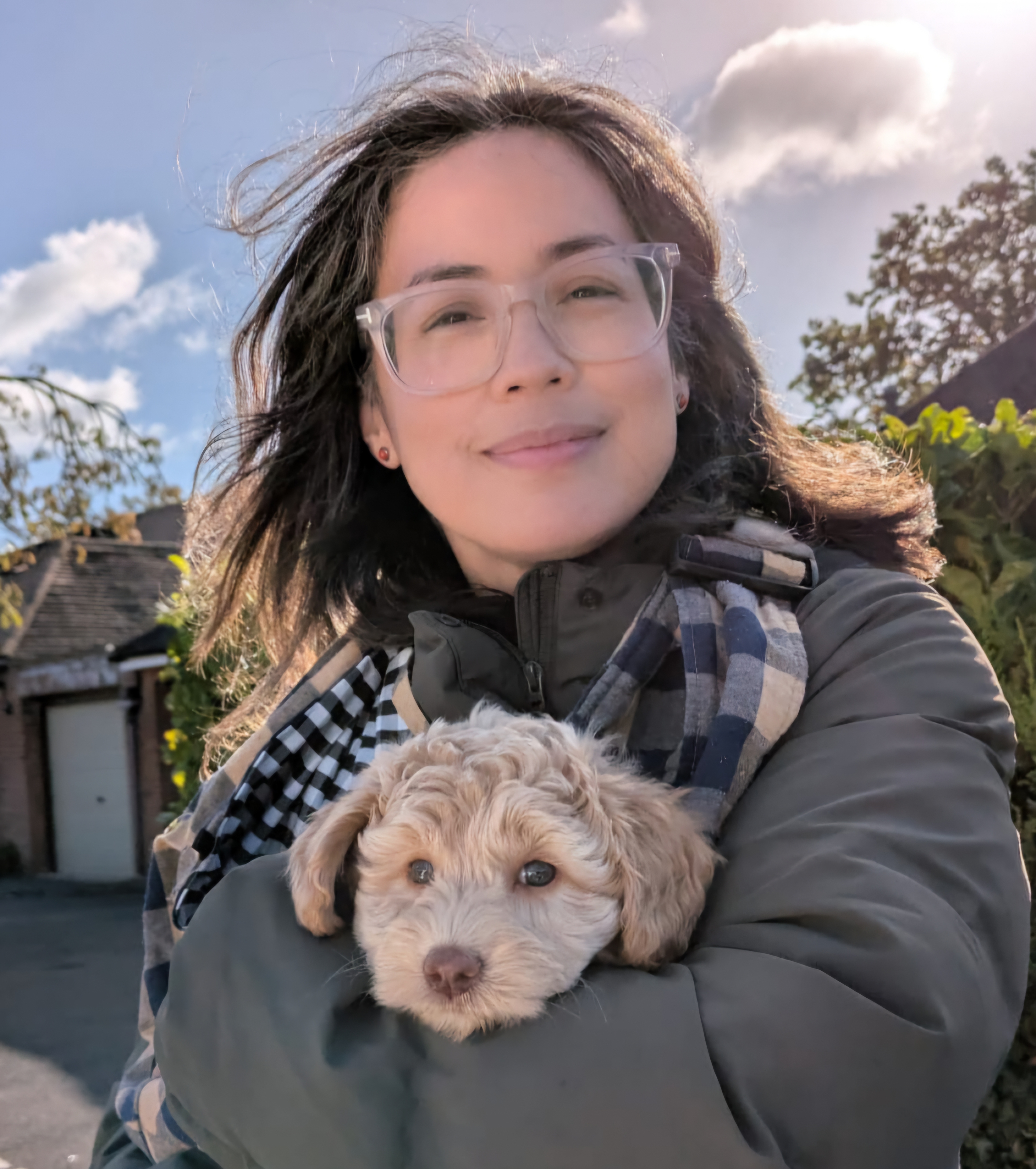 A person in clear glasses holds a small puppy in her arms