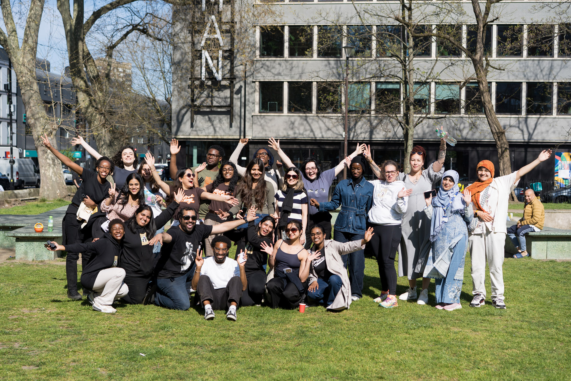 A group of students standing in the park with their hands in the air