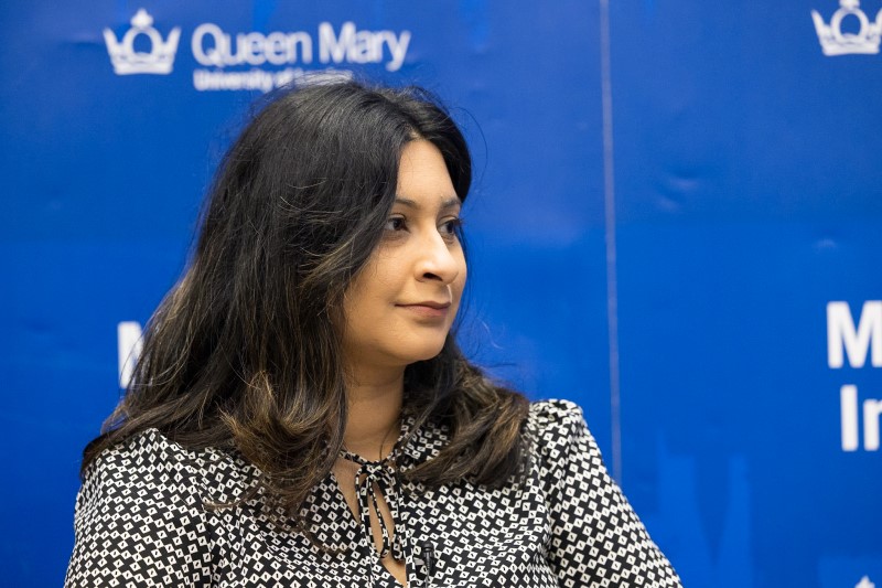 A photo of Farah Hussain speaking at a Mile End Institute event in front of a blue background