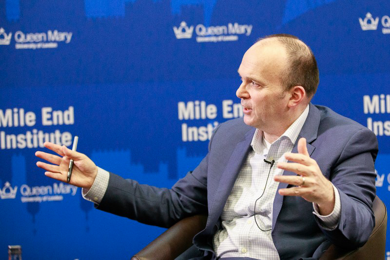 A photo of Philip Cowley speaking at an event in front of a blue banner for the Mile End Institute
