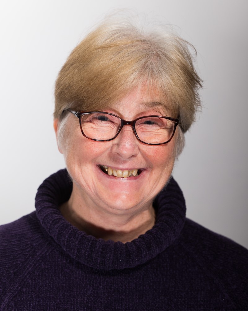 A photo of Kimberly Hutchings in front of a plain white background. She is wearing glasses and smiling.