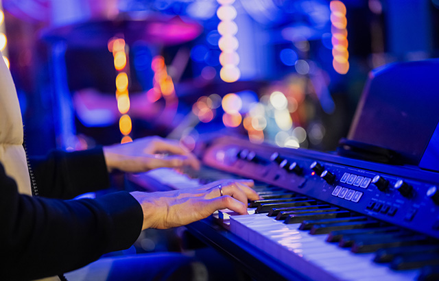 Musician pianist playing keyboard digital piano with blue blurred background with lights in concert.