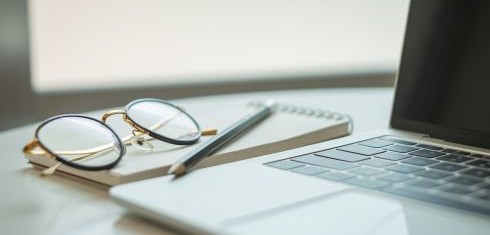 A laptop keyboard with a notebook and pen