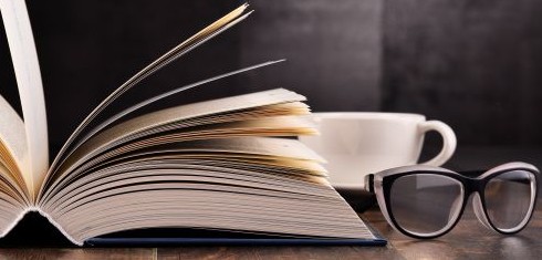 A cup of coffee next to an open book and a pair of glasses