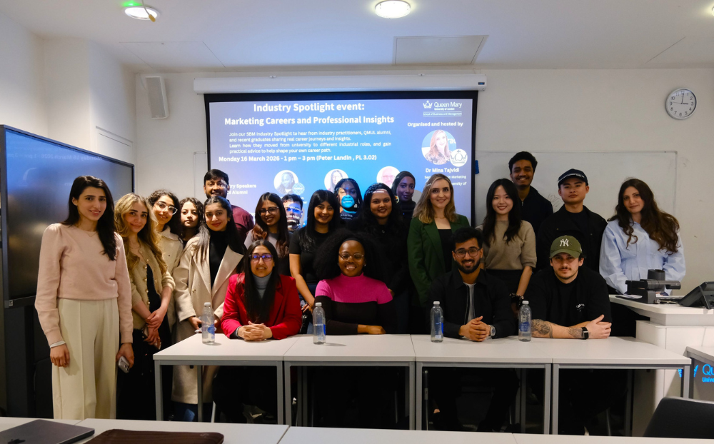 An image of students in a classroom along with guest speakers standing in front of a powerpoint and smiling