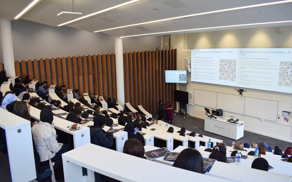 Image of lecture theatre with the backs of the heads of attendees sitting and watching an academic talk at the rise up event