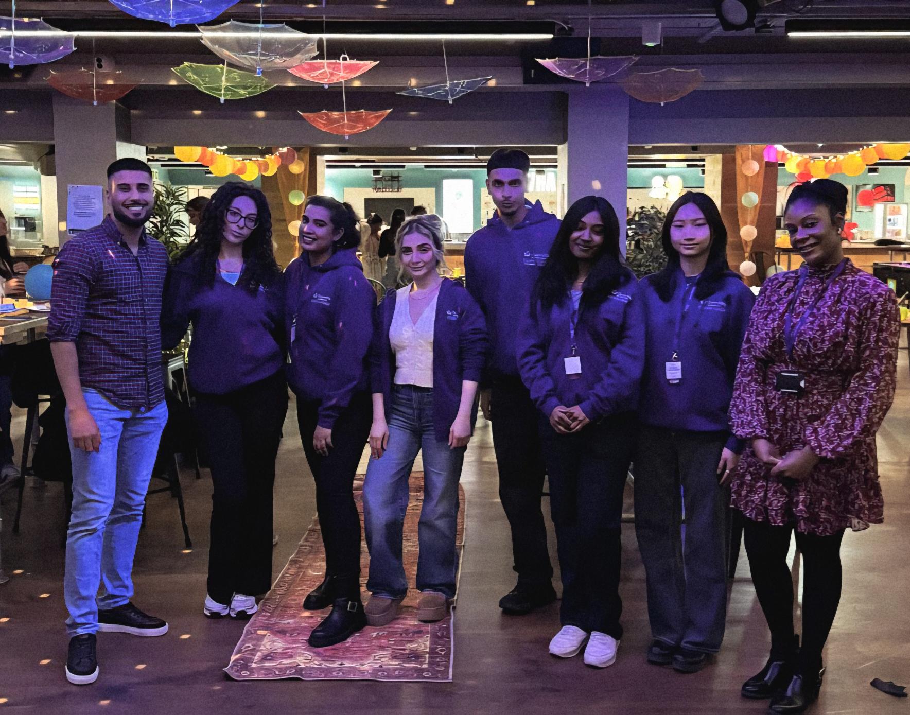 students and staff standing smiling inside a bar with umbrellas hanging upside down and tables on either side