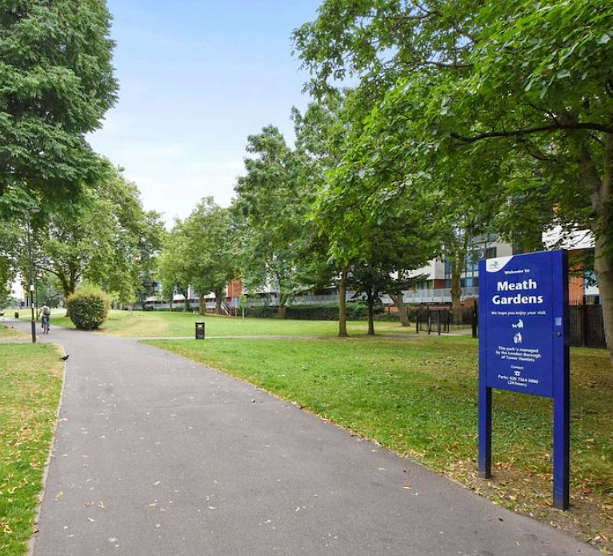 A photo of a park lane with trees on either side and a blue sign.
