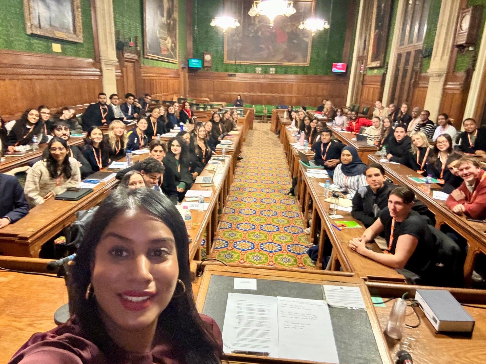 A selfie photograph my MP Uma Kumaran in the houses of parliament with Queen Mary students in the background