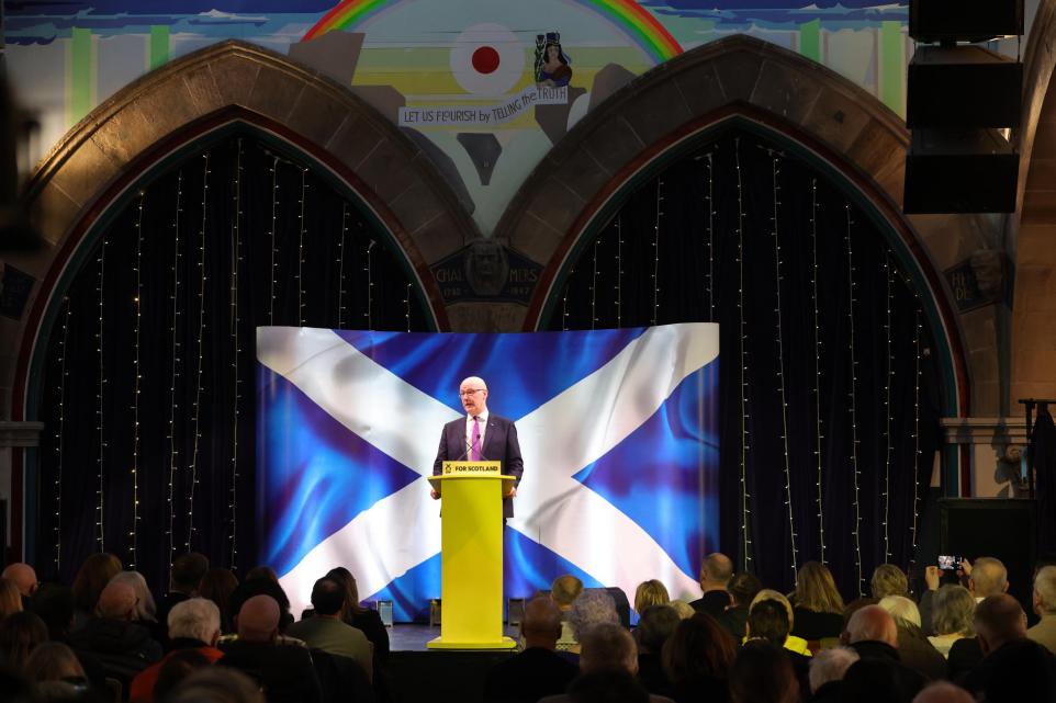an image of a man standing in front of an illuminated image of a saltire or scottish flag
