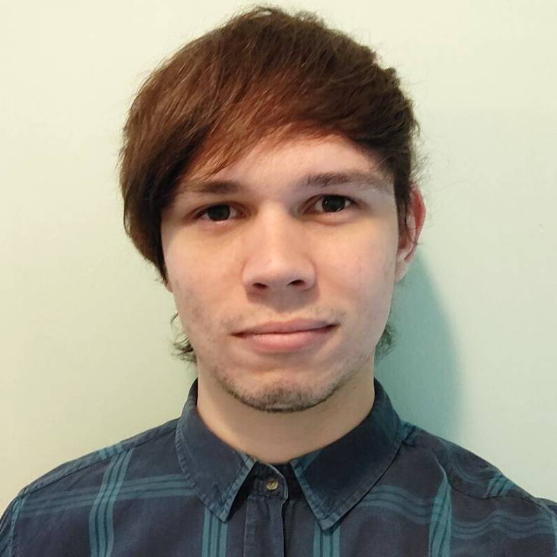 Bradley Desborough looking at the camera. Wearing a shirt and standing in front of a white background.