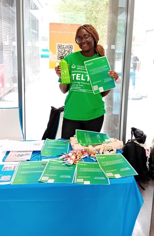 A student behind a desk holding a TELT bottle and paper in a green TELT t-shirt.
