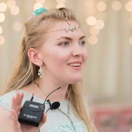 Jade Mills in a light green dress looking to the right. There are fairy lights in the background and a white curtain.