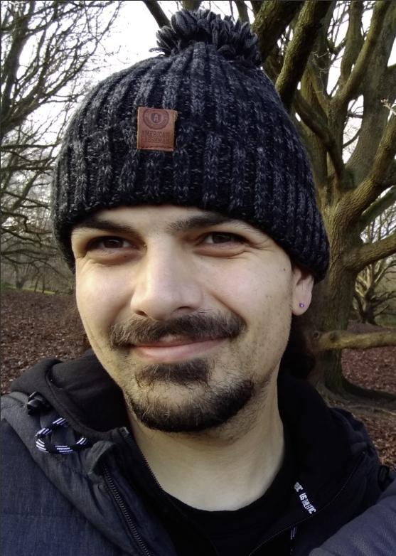 Pedro smiling and looking at the camera wearing a wooly hat. They are stood outside with a tree behind them.