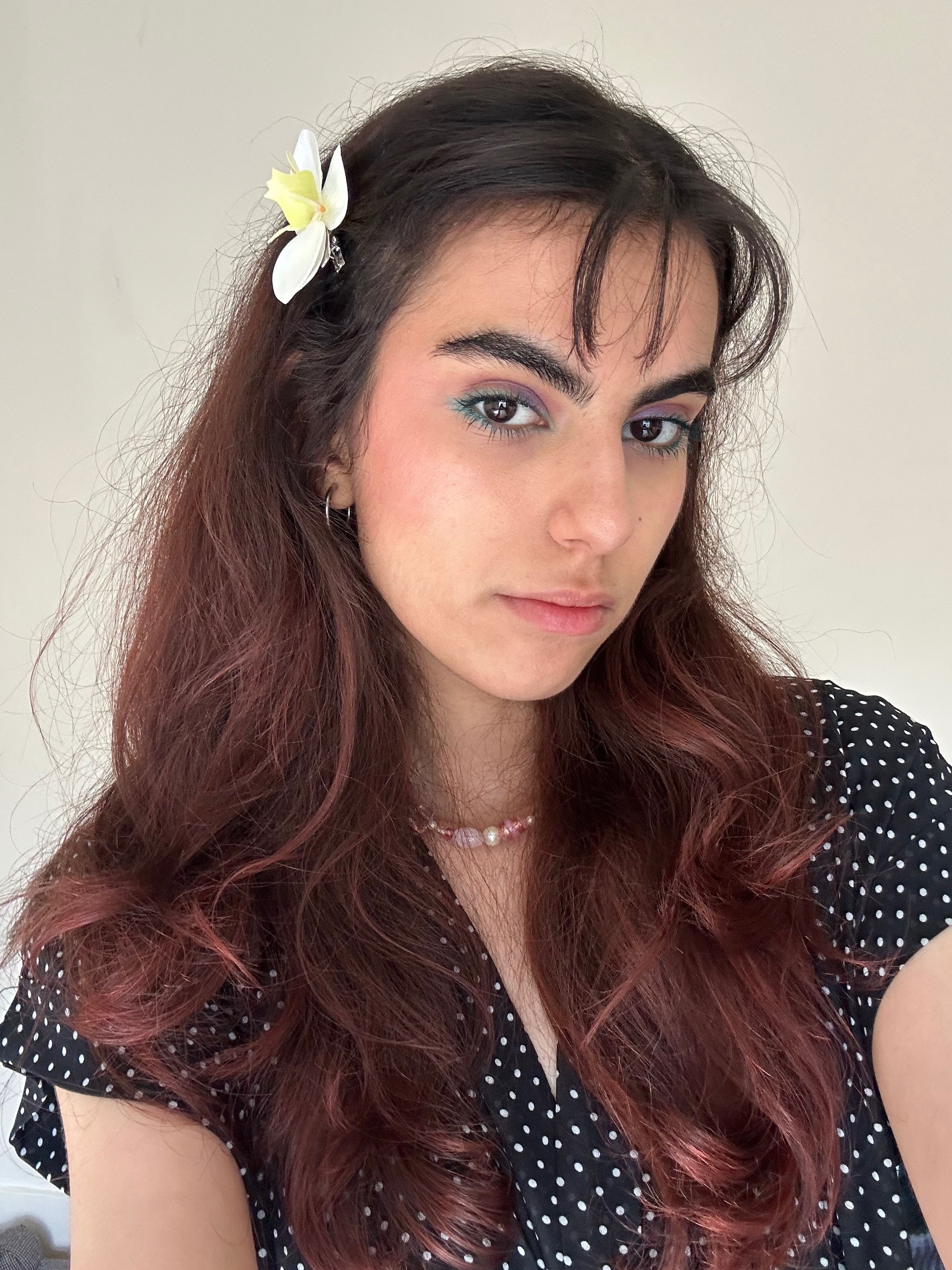 Stefania, TEL Ambassador she has a flower in her long hair.She is wearing a dark top and looking at the camera.