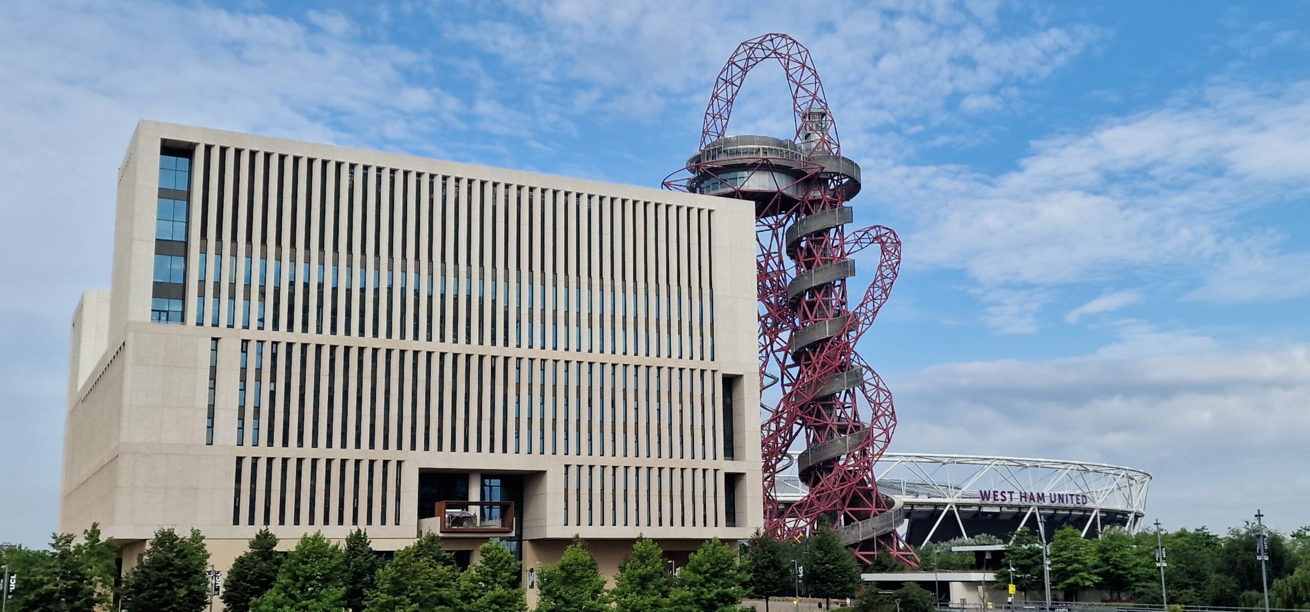 UCL East campus and exterior view of the building and the tourist attraction  ArcelorMittal Orbit is visible. There is a blue sky.