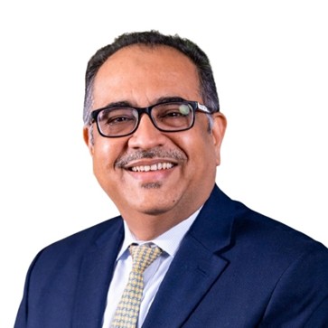 Parvaiz Dalal smiling, wearing a blue suit and glasses.