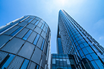 A view looking up from the ground at glass office buildings and a blue sky.